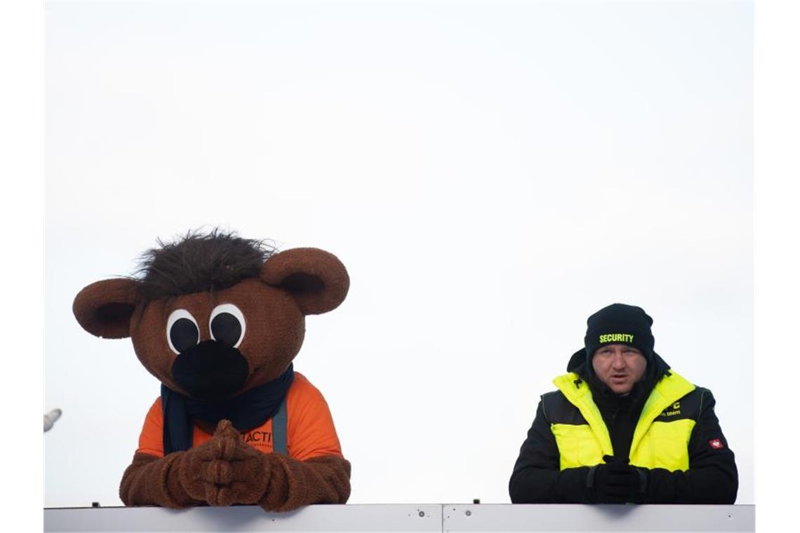 WM-Maskottchen Bobby und ein Sicherheitsmann beobachten die Zieleinfahrt in Altenberg. Foto: Sebastian Kahnert/dpa-Zentralbild/dpa