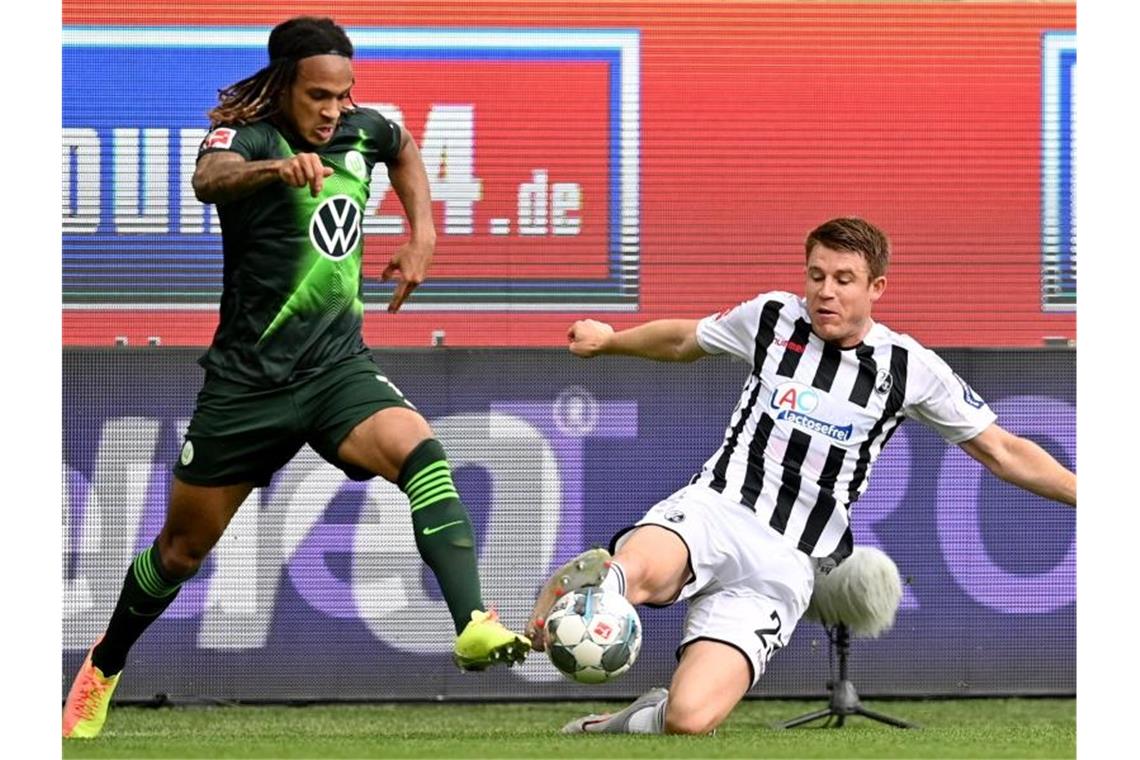 Wolfsburgs Kevin Mbabu (l) im Duell mit Dominique Heintz vom SC Freiburg. Foto: Sascha Steinbach/epa Pool/dpa