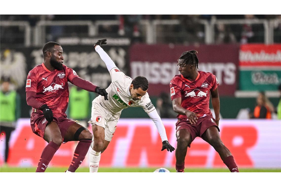 RB Leipzig mit Nullnummer in Augsburg WWK-Arena. Leipzigs Lutsharel Geertruida (l) und Leipzigs Amadou Haidara (r) in Aktion mit Augsburgs Alexis Claude-Maurice (M).