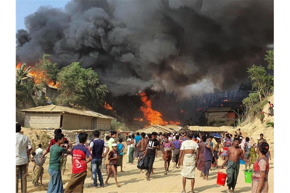 Zahlreiche Menschen betrachten den Rauch, der über dem in Flammen stehenden Lager aufsteigt. Foto: Shafiqur Rahman/AP/dpa