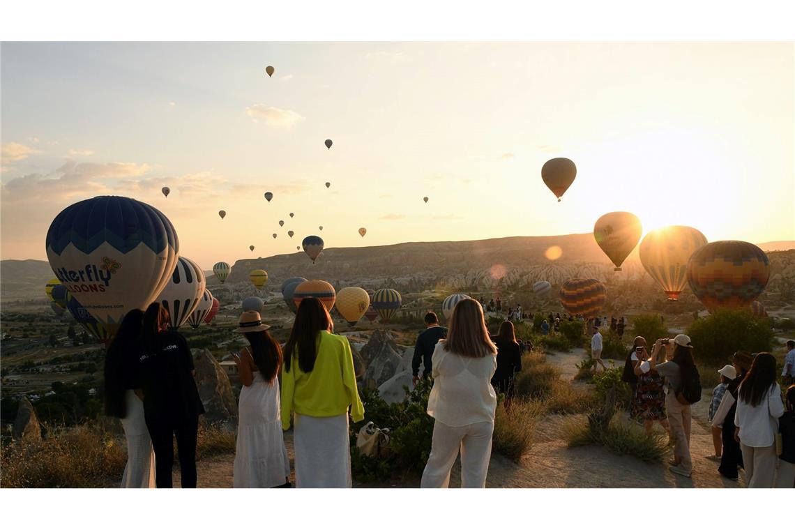 Zahlreiche Schaulustige bestaunen wie im türkischen Kappadokien Heißluftballons über Gesteinsformation Kappadokien fliegen.