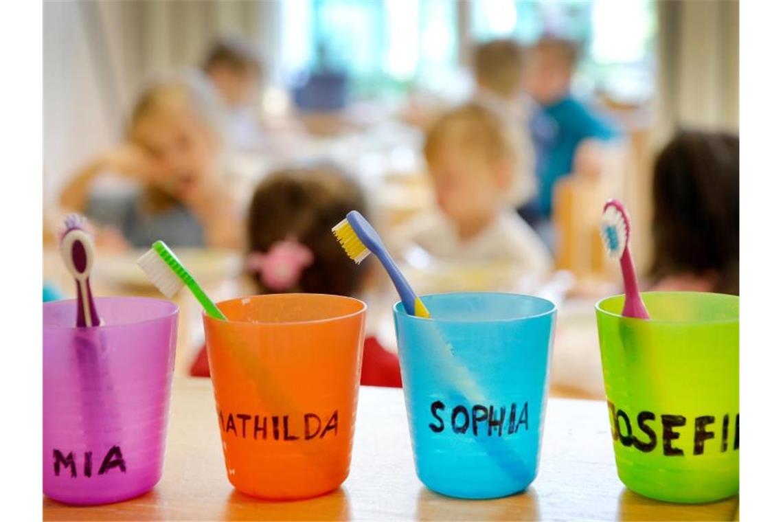 Zahnbürsten und Zahnputzbecher mit den Vornamen der Kinder stehen in einer Kindertagesstätte auf einem Tisch. Foto: Monika Skolimowska/dpa