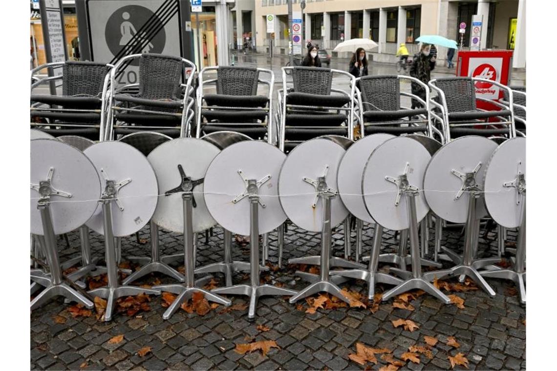 Zusammengestellte Stühle und Tische stehen vor einem Café in München. Foto: Peter Kneffel/dpa