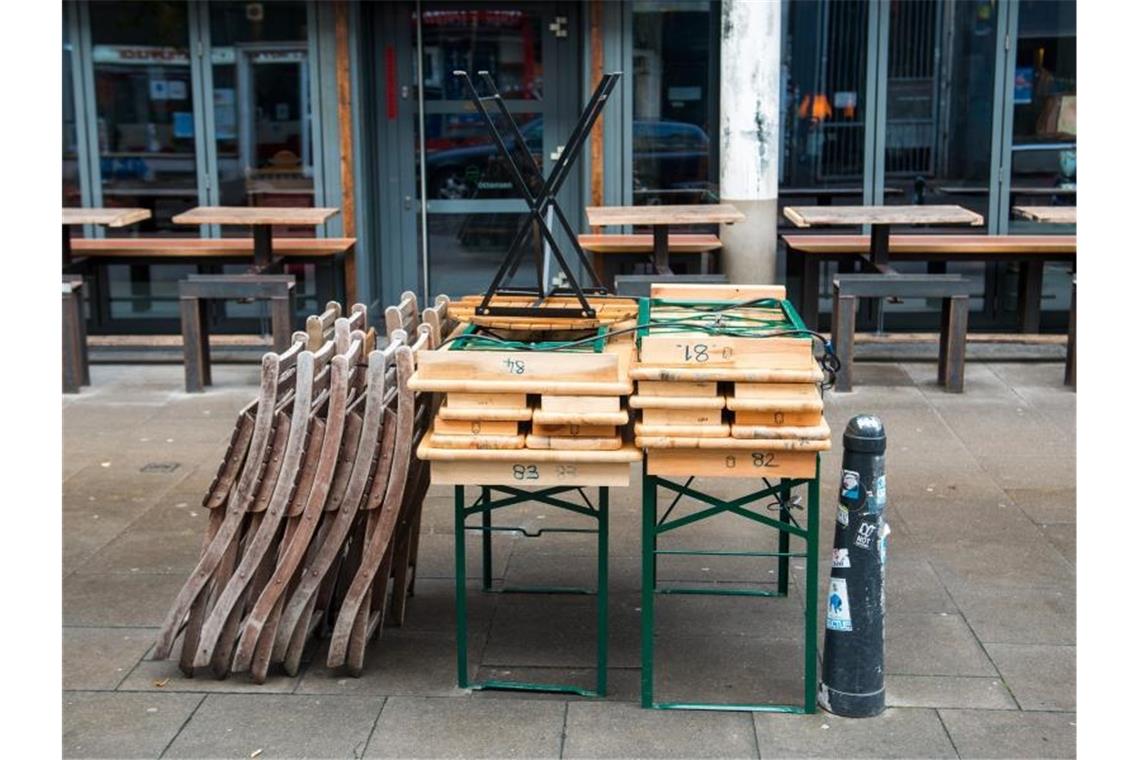 Zusammengestellte Tische und aufgestapelte Stühle stehen vor einem geschlossenen Café in Hamburg. Foto: Daniel Bockwoldt/dpa