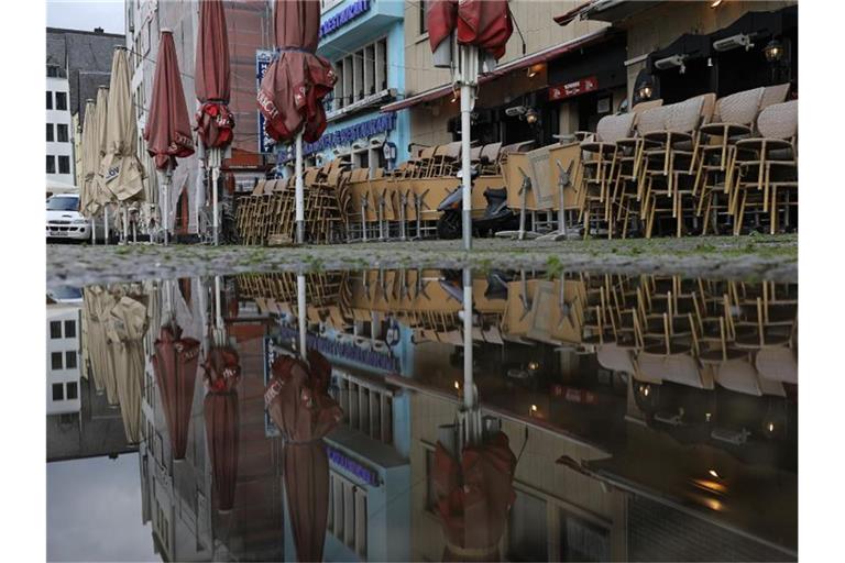 Zusammengestellte Tische und Stühle vor einem geschlossenen Lokal in Köln. Foto: Oliver Berg/dpa