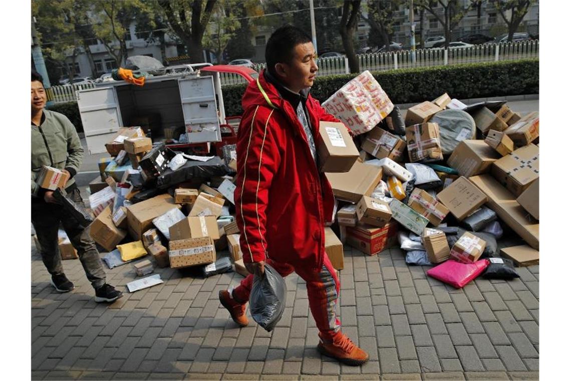 Zusteller sortieren Pakete, die sich an einem Abholpunkt in der Nähe eines Wohnhauses in Peking stapeln. Foto: Andy Wong/AP/dpa