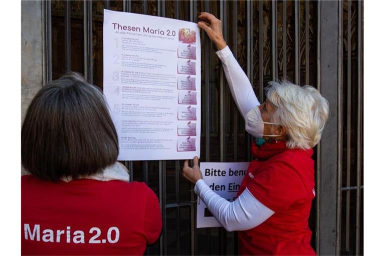 Zwei Aktivistinnen der katholischen Reforminitiative Maria 2.0 hängen ein Plakat mit ihren Thesen an das Hauptportal des Münsters. Foto: Philipp von Ditfurth/dpa