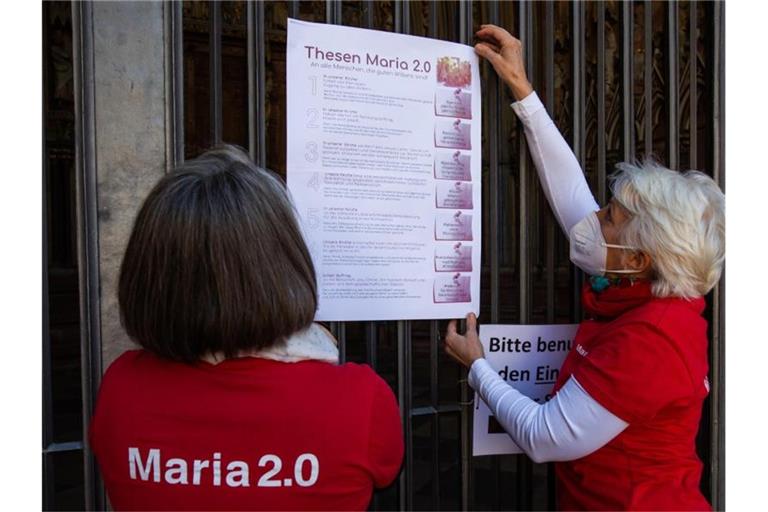 Zwei Aktivistinnen der katholischen Reforminitiative Maria 2.0 hängen ein Plakat mit ihren Thesen an das Hauptportal des Freiburger Münsters. Foto: Philipp von Ditfurth/dpa