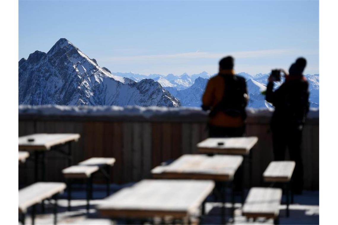 Zwei Besucher fotografieren von der Zugspitze aus das Panorama des Wettersteingebirges. Nach gut eineinhalbjähriger Pause wegen Corona sollen dort wieder Lifte laufen und Skifahrer ihre Schwünge ziehen. Foto: Angelika Warmuth/dpa