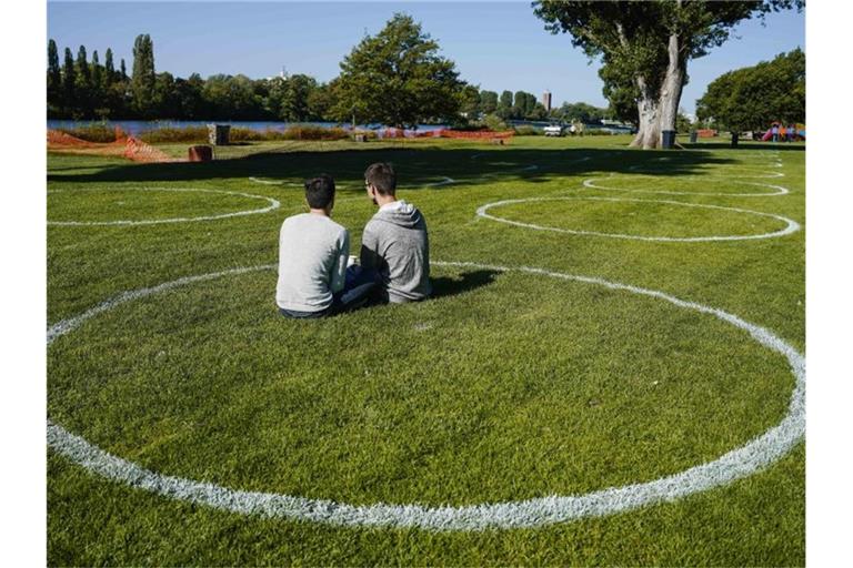 Zwei Besucher sitzen auf der Neckarwiese in einem mit spezieller Farbe gemalten Kreis. Foto: Uwe Anspach/dpa