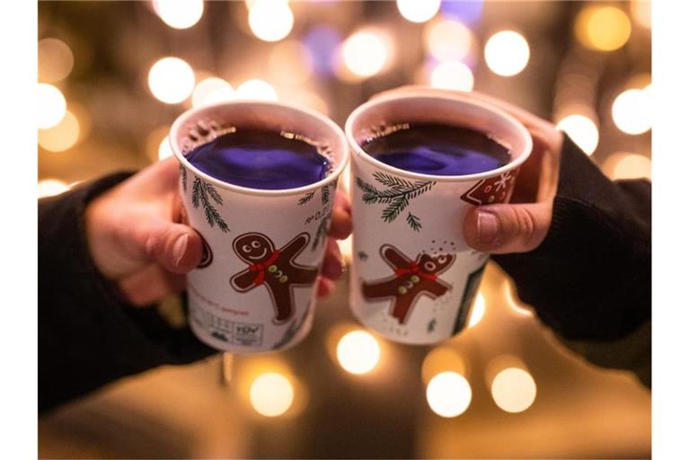 Zwei Besucherinnen eines Weihnachtsmarktes stoßen mit Glühwein an. Foto: Christoph Schmidt/dpa/Symbolbild