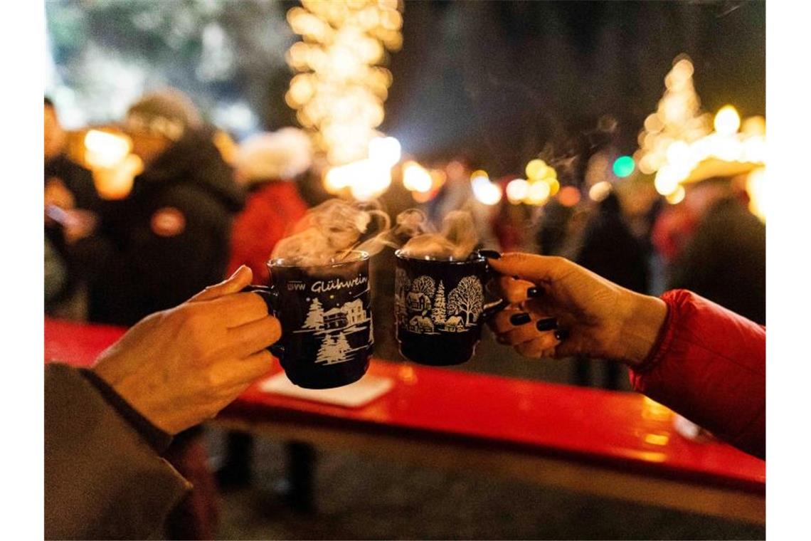 Zwei Besucherinnen stoßen in der Weihnachtszeit 2019 auf einem Weihnachtsmarkt mit Glühwein an. Foto: Philipp von Ditfurth/dpa/Archivbild