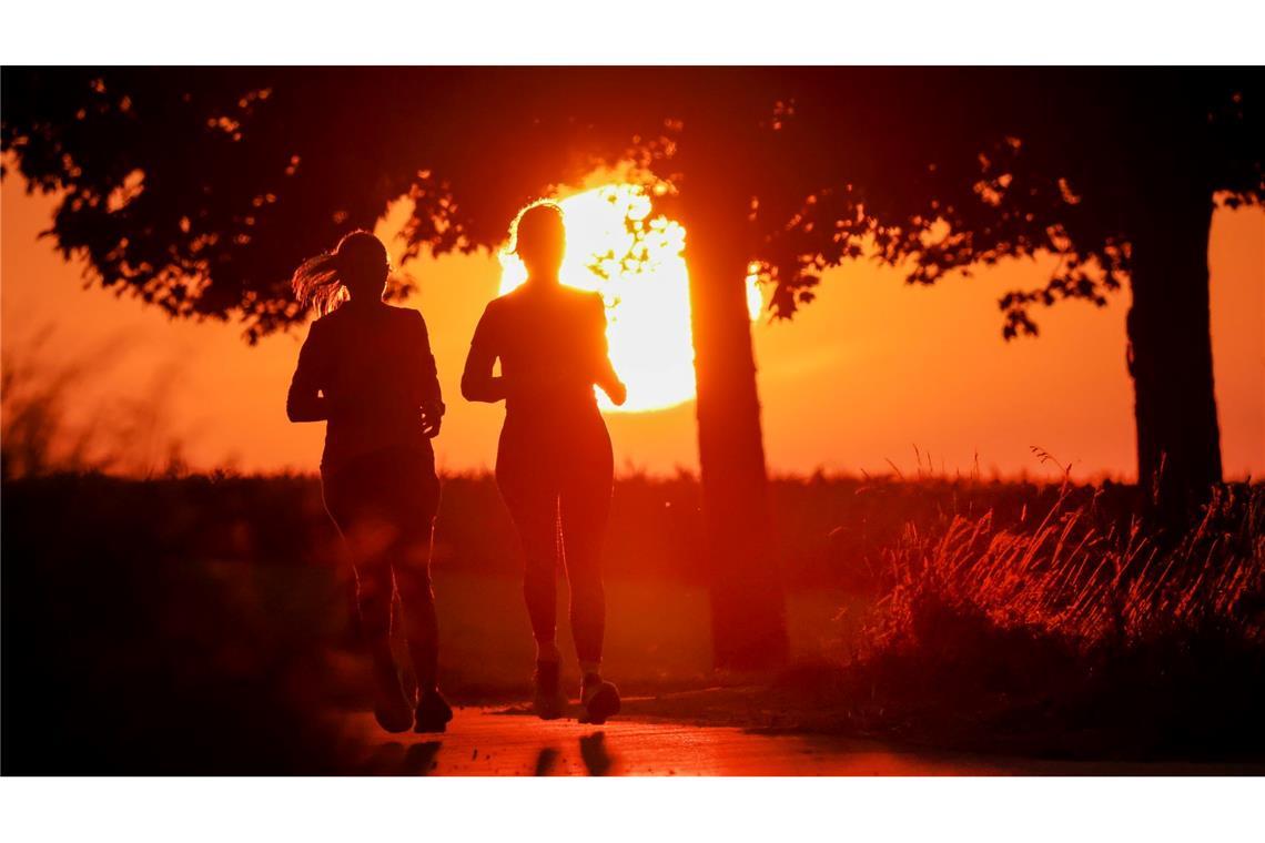 Nach Hitze-Wochenende: Gewitter und viel Wind erwartet Zwei Frauen joggen am Morgen, während hinter ihnen die Sonne aufgeht.