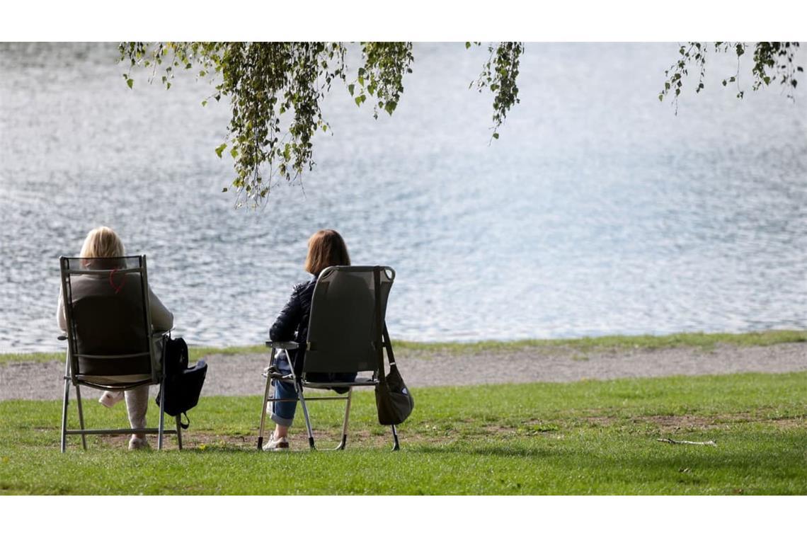 Zwei Frauen sitzen auf Klappstühlen an einem See in der Sonne. (Symbolbild)