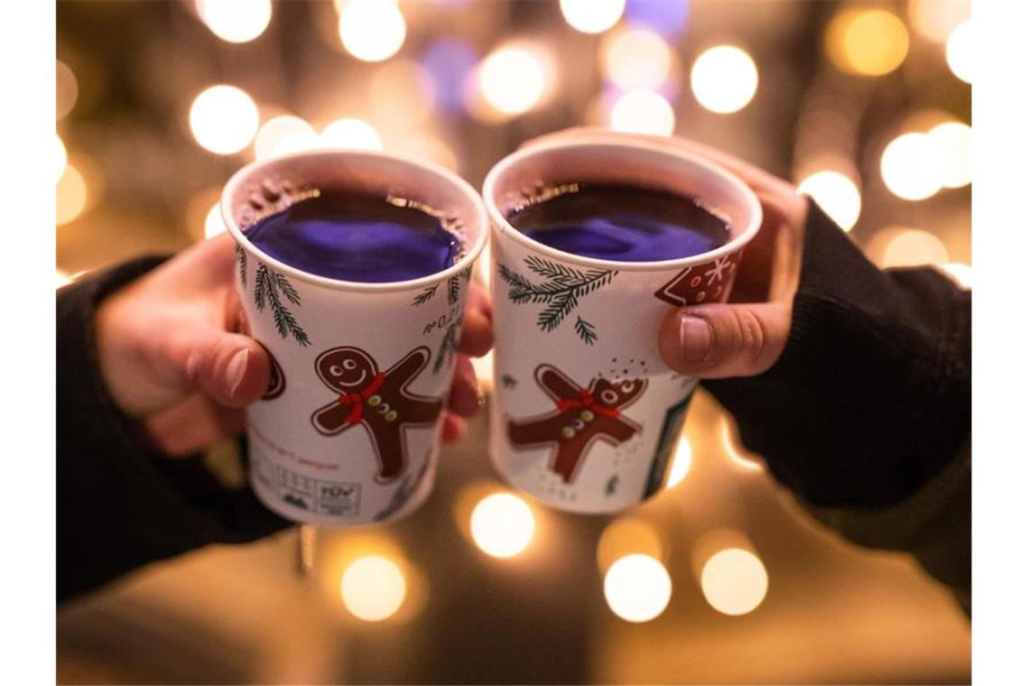 Zwei Frauen stoßen mit Glühwein in Bechern auf dem Weihnachtsmarkt an. Foto: Christoph Schmidt/dpa