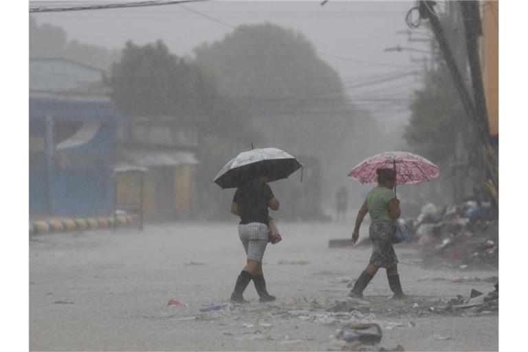 Zwei Frauen überqueren bei starkem Regen eine Straße in La Lima in Honduras. Foto: Delmer Martinez/AP/dpa