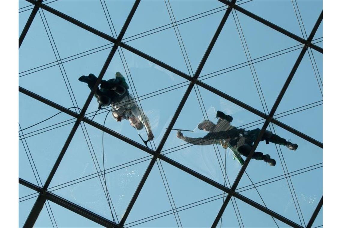 Zwei Gebäudereiniger putzen in rund 27 Metern Höhe ein gläsernes Dach. Foto: Sebastian Kahnert/zb/dpa