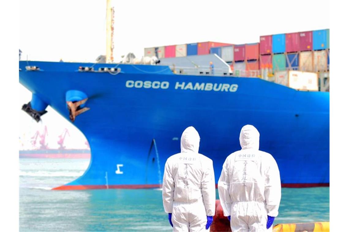Zwei Hafenmitarbeiter in Qingdao beobachten den Containerfrachter „Cosco Hamburg“. Foto: Yufangping/SIPA Asia via ZUMA Wire/dpa