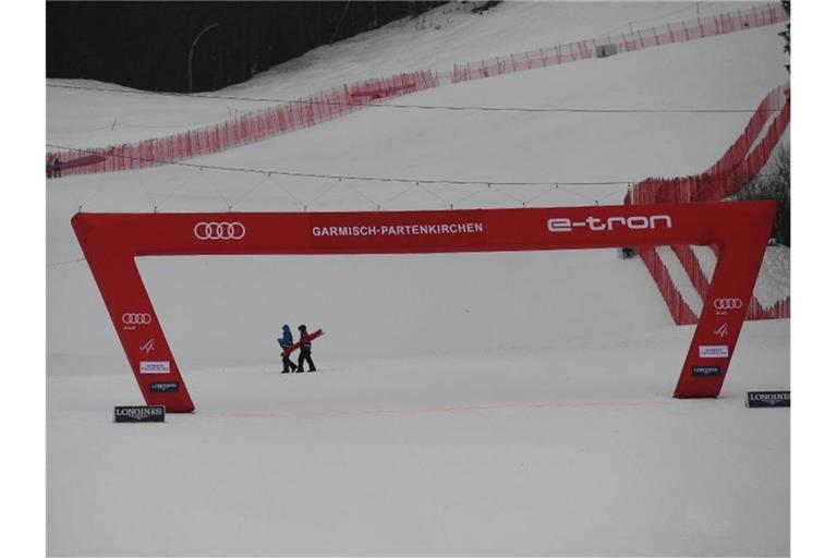 Zwei Helfer gehen in Garmisch hinter dem Zielbogen vorbei. Das zweite Training wurde wegen zu schlechtem Wetters abgesagt. Foto: Angelika Warmuth/dpa