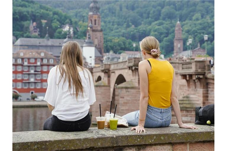 Zwei junge Frauen sitzen an der Alten Brücke. Foto: Uwe Anspach/dpa/Archivbild