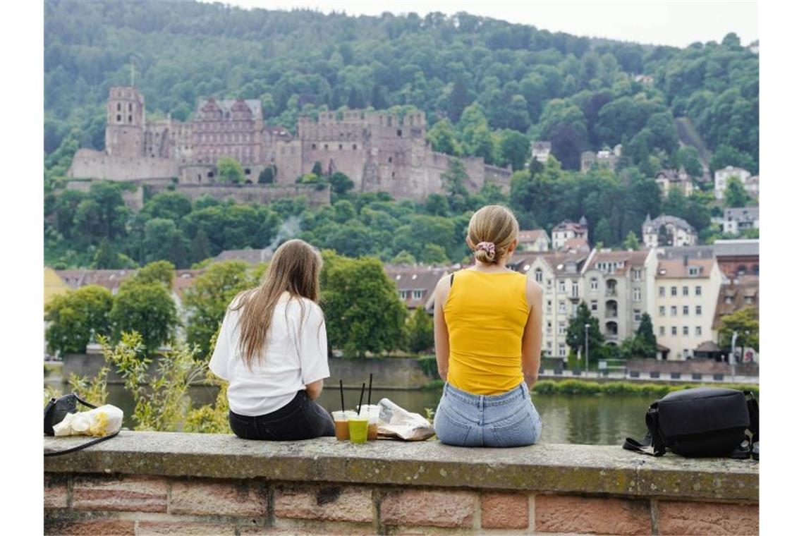 Heidelberg kann Bundesnotbremse lockern Zwei junge Frauen sitzen mit Blick auf das Heidelberger Schloss an der Alten Brücke. Foto: Uwe Anspach/dpa/Archivbild