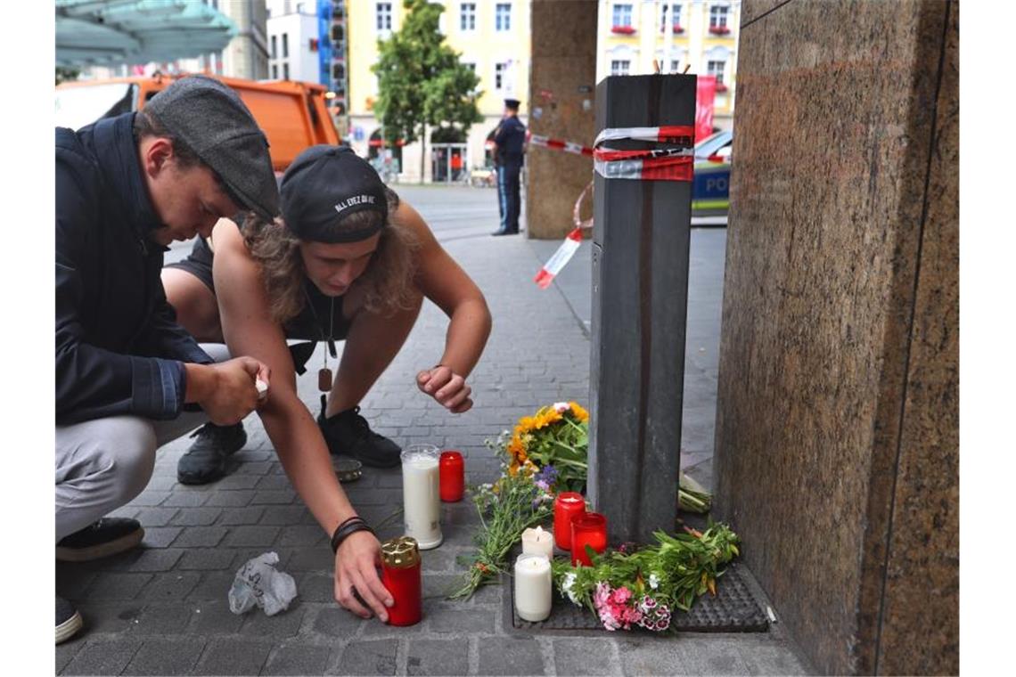 Messerangriff in Würzburg - Auf der Suche nach dem Motiv Zwei junge Männer entzünden vor einem geschlossenen und abgesperrten Geschäft in der Würzburger Innenstadt eine Kerze. Foto: Karl-Josef Hildenbrand/dpa