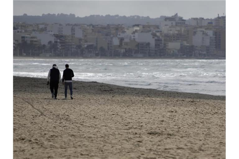 Zwei Männer gehen am Strand von Arenal über den Sand. Foto: Clara Margais/dpa