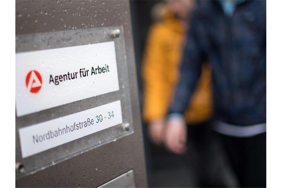 Weniger Arbeitslose im Juni Zwei Männer gehen hinter dem Logo der Agentur für Arbeit vorbei. Foto: Sebastian Gollnow/Archivbild