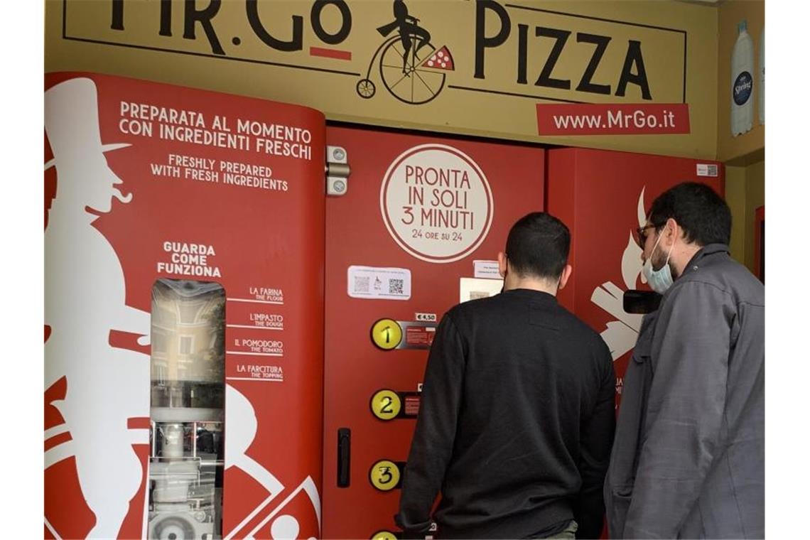 Pizza-Automat spaltet kulinarische Meinung in Rom Zwei Männer kaufen sich am Pizza-Automaten „Mr. Go“ etwas zu essen. Foto: Johannes Neudecker/dpa