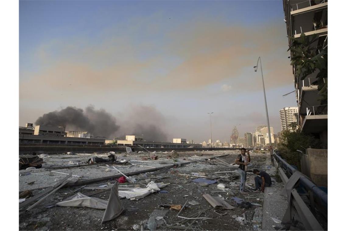 Zwei Männer stehen an einer mit Trümmern übersäten Straße. Foto: Hassan Ammar/AP/dpa