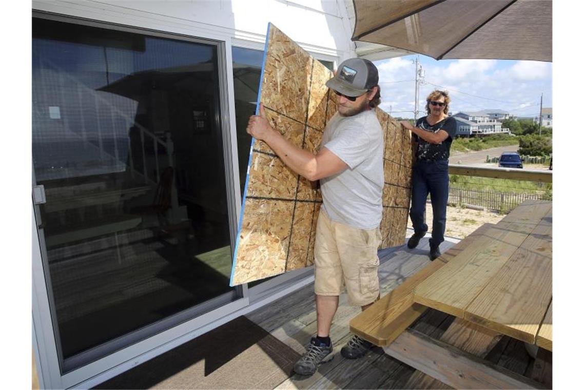 Zwei Männer wollen in Charlestown im US-Bundesstaat Rhode Island die Scheiben eines Hauses mit einer Spanplatte sichern. Foto: Stew Milne/AP/dpa