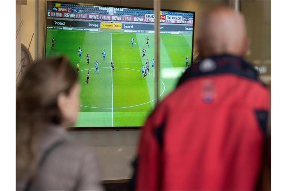 Zwei Menschen verfolgen außerhalb einer Bar ein Fußballspiel. Foto: Silas Stein/dpa/Symbolbild