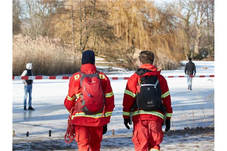 Zwei Mitglieder der Deutschen Lebens-Rettungs-Gesellschaft (DLRG) laufen auf einem vereisten See. Foto: Georg Wendt/dpa