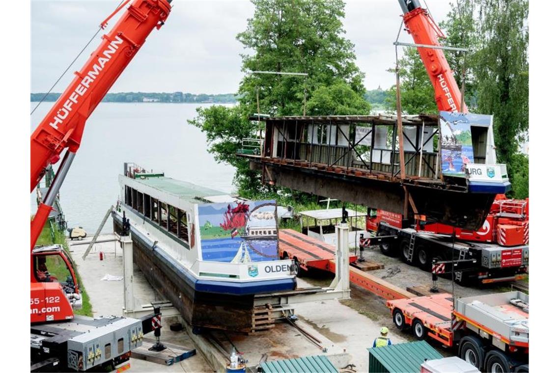 Zwei Mobilkrane heben ein Teilstück des längsseitig zersägten Fahrgastschiffes „MS Oldenburg“ am Zwischenahner Meer auf einen Tieflader. Foto: Hauke-Christian Dittrich/dpa