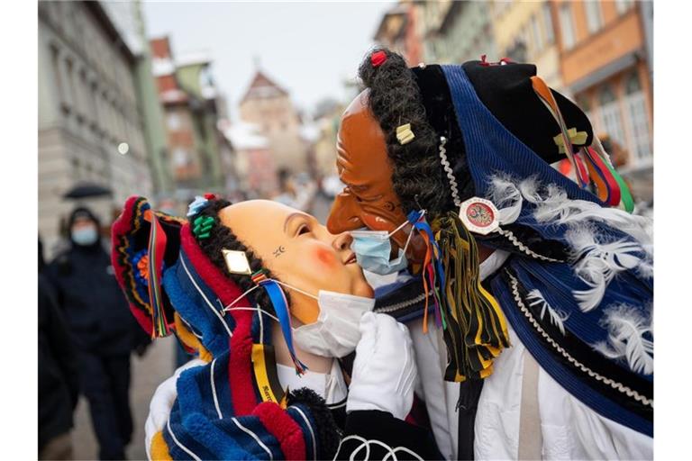 Zwei Narren mit OP-Masken über ihren Gesichtsmasken küssen sich am Fastnachtsmontag. Foto: Sebastian Gollnow/dpa