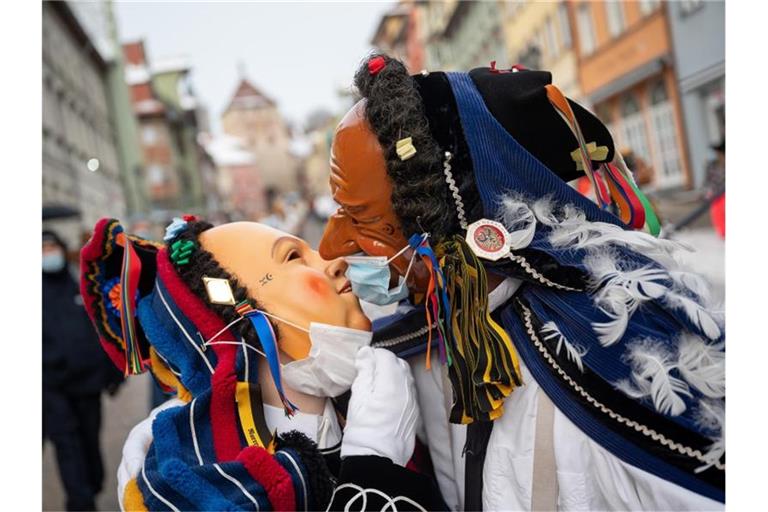 Zwei Narren mit OP-Masken über ihren Gesichtsmasken küssen sich am Fastnachtsmontag. Foto: Sebastian Gollnow/dpa