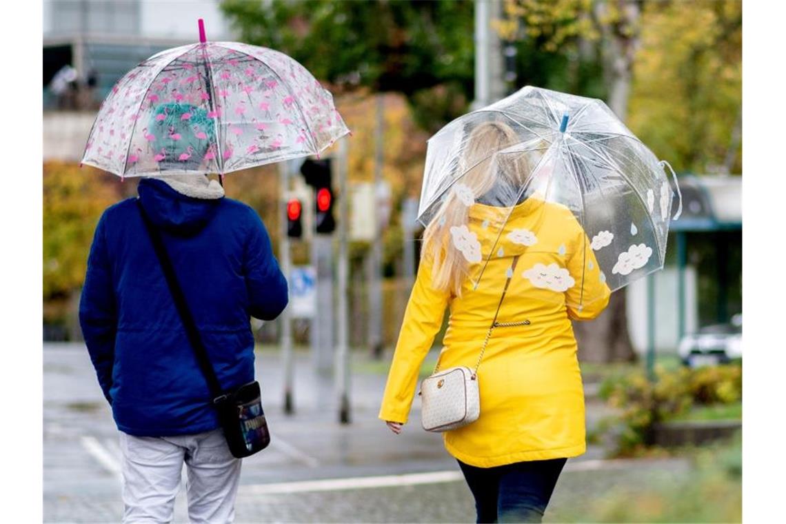 Zwei Passanten gehen mit Regenschirmen durch die Stadt. Foto: Hauke-Christian Dittrich/dpa/Archivbild
