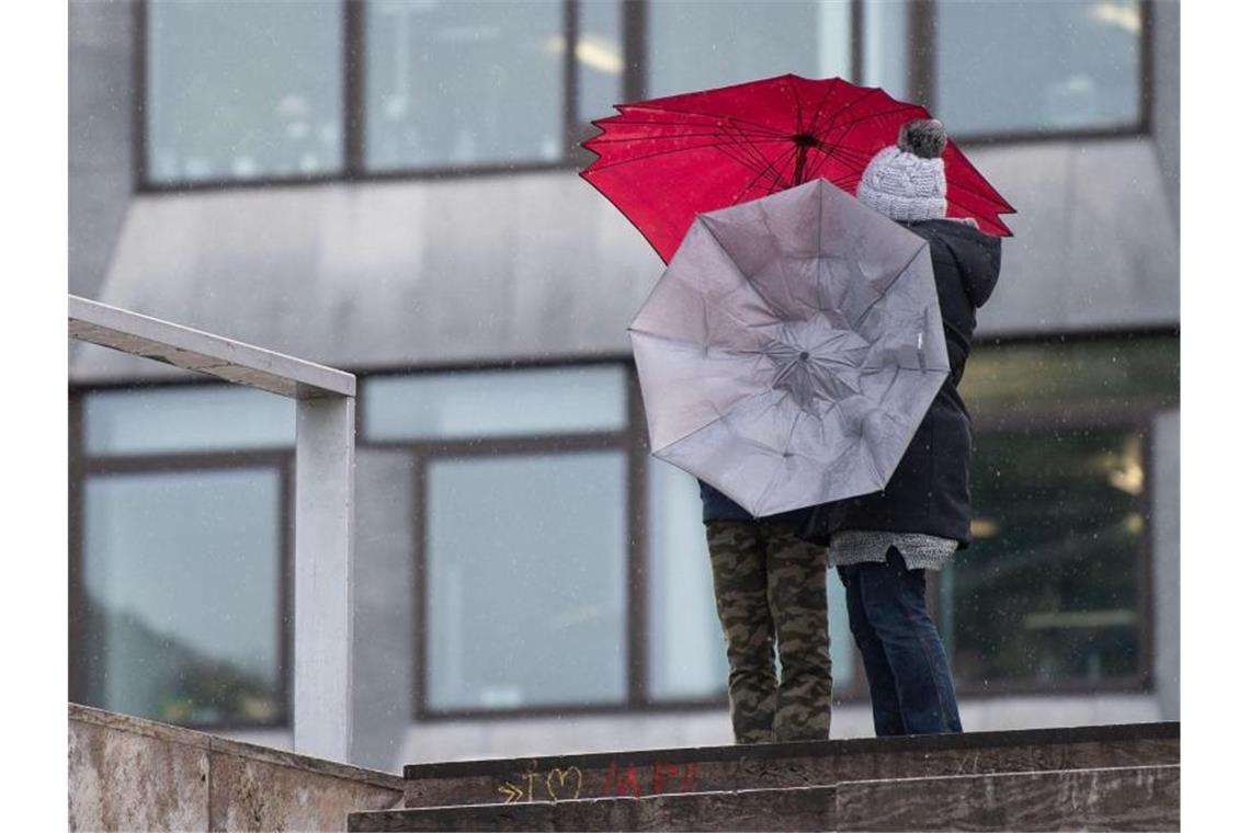 Zwei Passanten hantieren mit ihren Regenschirmen im Wind. Foto: Marijan Murat/Archivbild