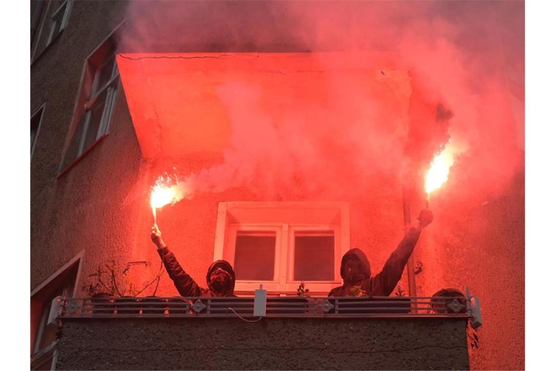 Zwei Personen halten während einer Demonstration linker und linksradikaler Gruppen durch Wedding zwei brennende Rauchfackeln auf einem Balkon. Foto: Christophe Gateau/dpa
