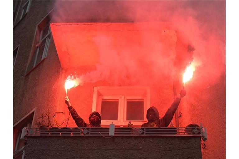 Zwei Personen halten während einer Demonstration linker und linksradikaler Gruppen durch Wedding zwei brennende Rauchfackeln auf einem Balkon. Foto: Christophe Gateau/dpa
