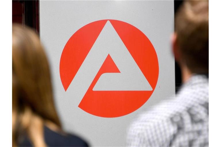 Zwei Personen stehen vor dem Logo der Agentur für Arbeit. Foto: Carsten Rehder/Archiv
