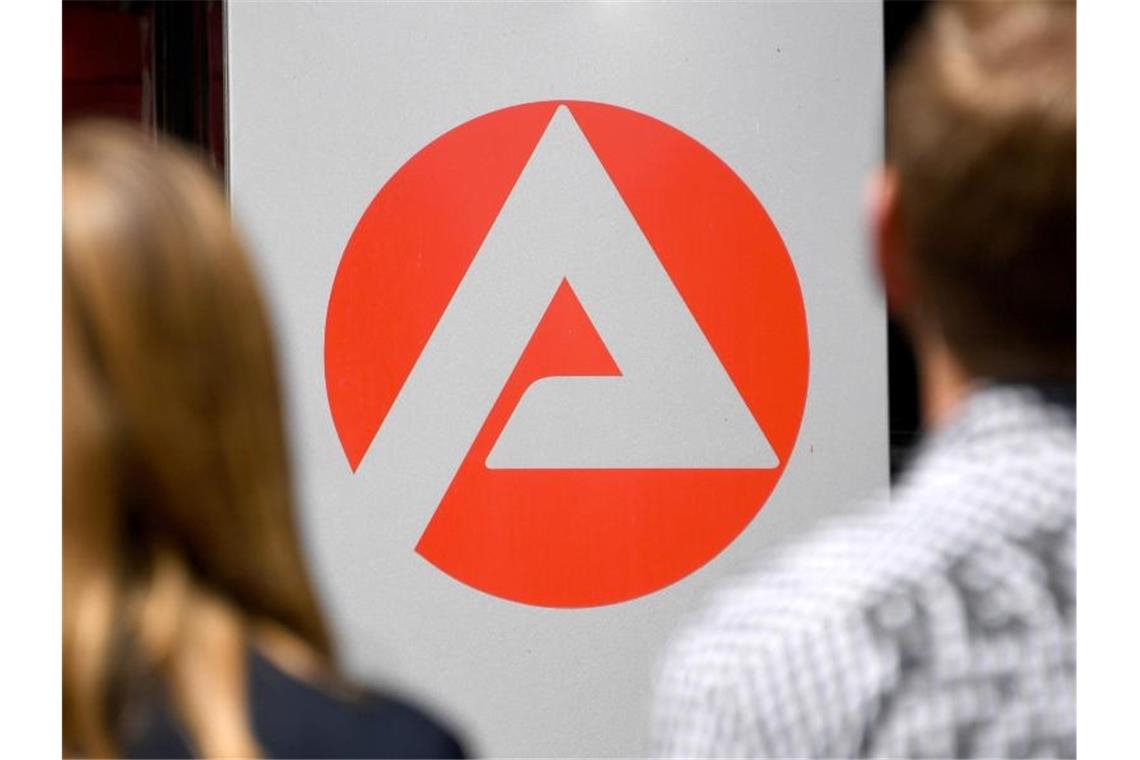 Zwei Personen stehen vor dem Logo der Agentur für Arbeit. Foto: Carsten Rehder/dpa/Archivbild