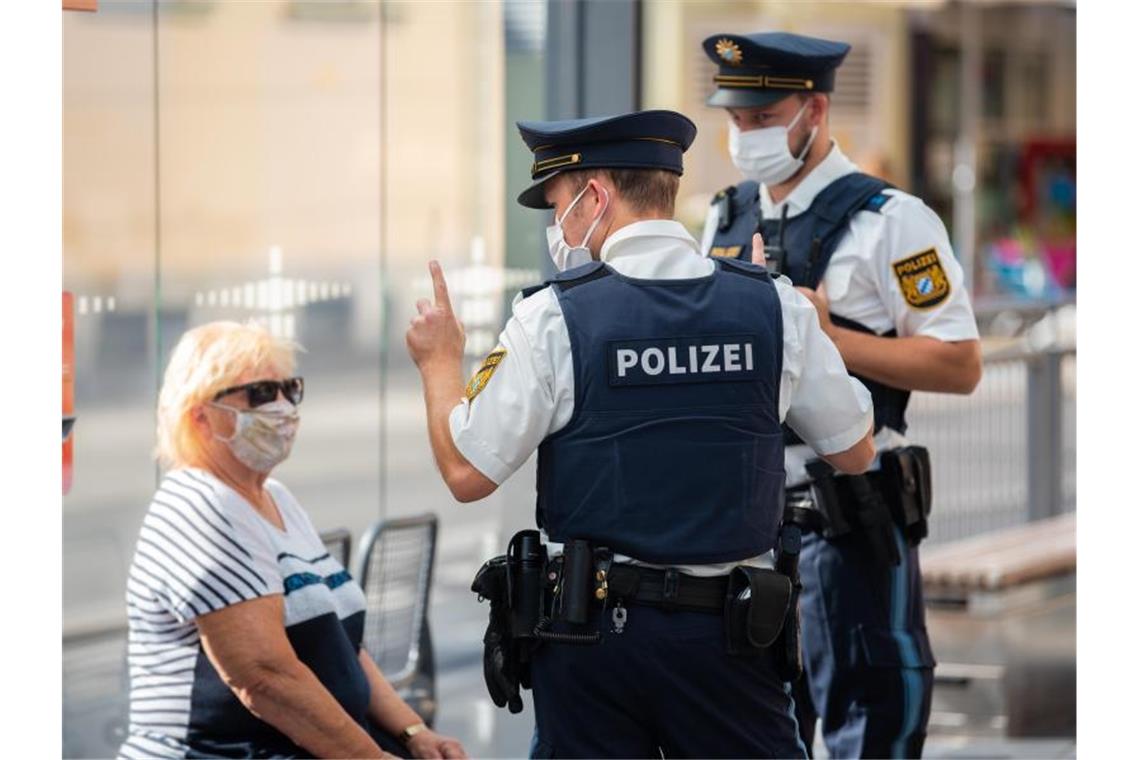 Zwei Polizisten nehmen an einer Tram-Haltestelle in Würzburg von einer Frau nach einem Verstoß gegen die Maskenpflicht im öffentlichen Nahverkehr die Personalien auf. Foto: Nicolas Armer/dpa