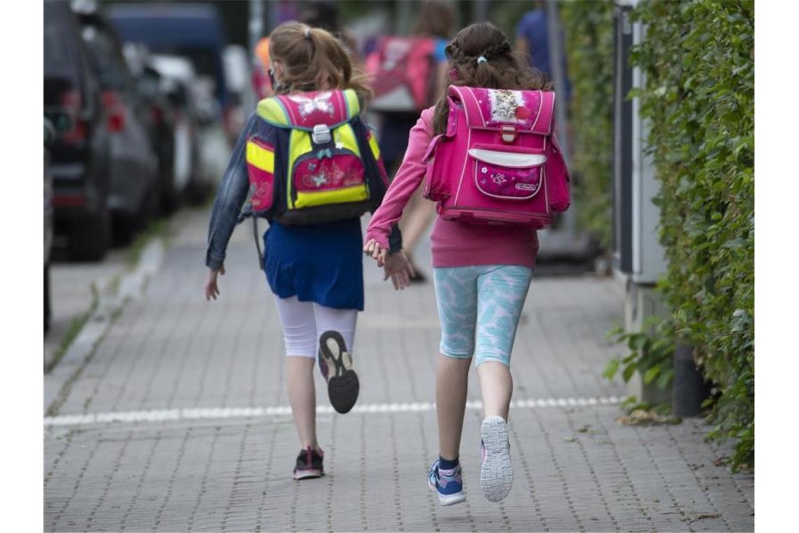 Zwei Schülerinnen einer Grundschule rennen mit einem Schulranzen auf dem Rücken die letzten Meter bis zum Schulhof. Foto: Boris Roessler/dpa