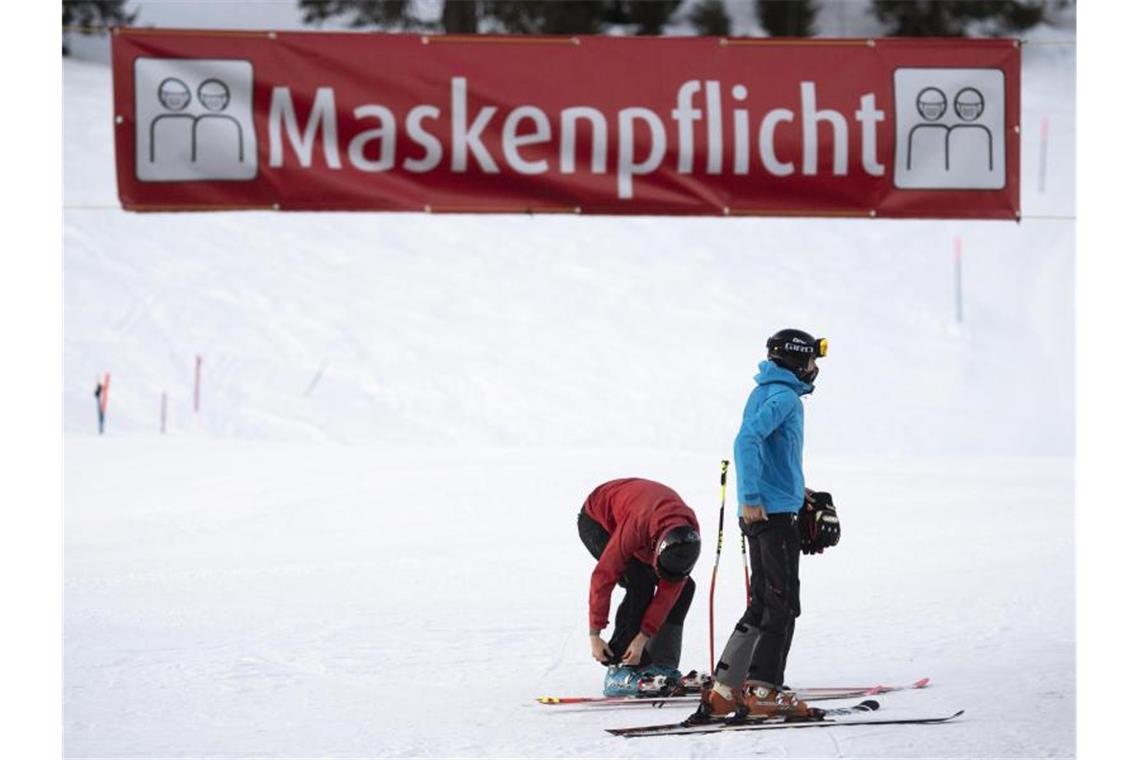 Zwei Skifahrer stehen unter einem Banner im Skigebiet Flumserberg, das auf die Maskenpflicht hinweist. Foto: Gian Ehrenzeller/KEYSTONE/dpa