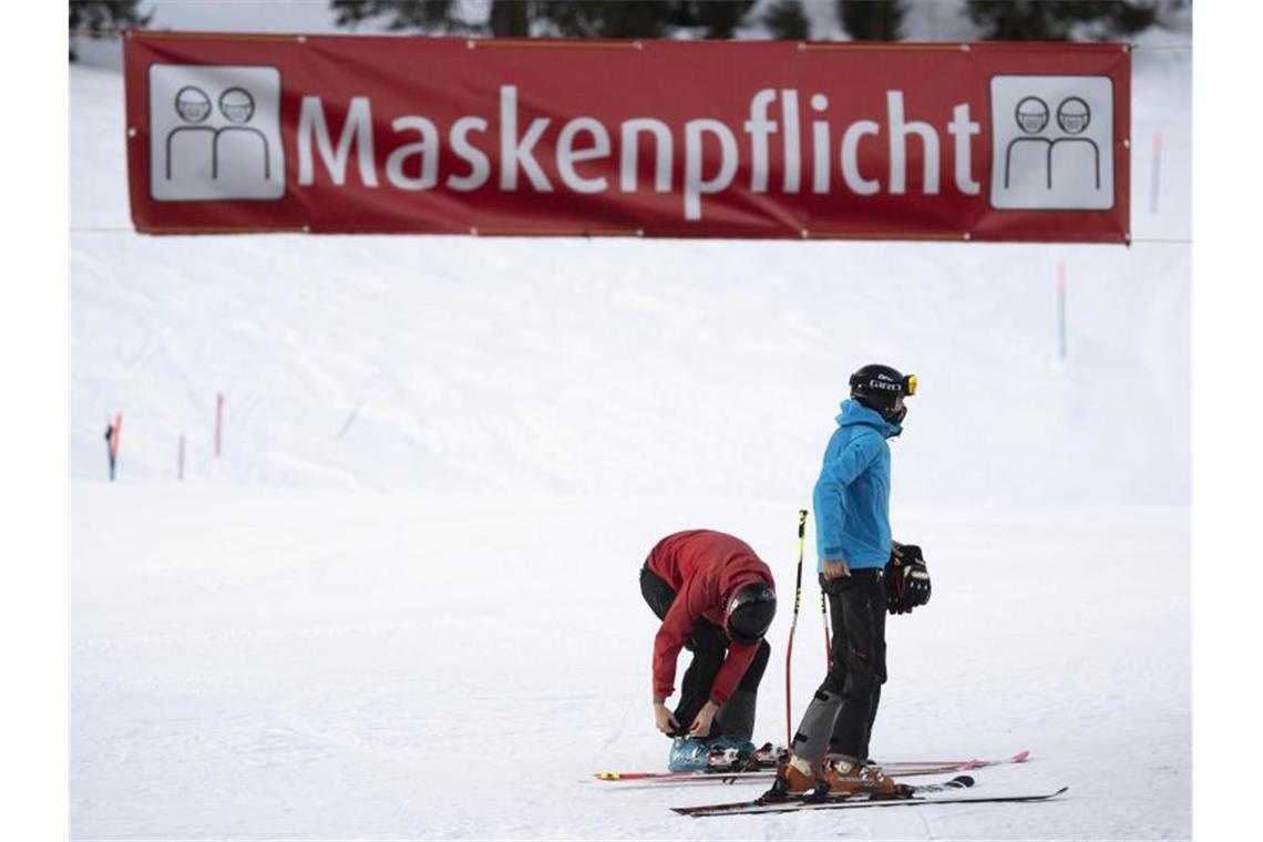 Österreich ab 26. Dezember in Lockdown Zwei Skifahrer stehen unter einem Banner im Skigebiet Flumserberg, das auf die Maskenpflicht hinweist. Foto: Gian Ehrenzeller/KEYSTONE/dpa