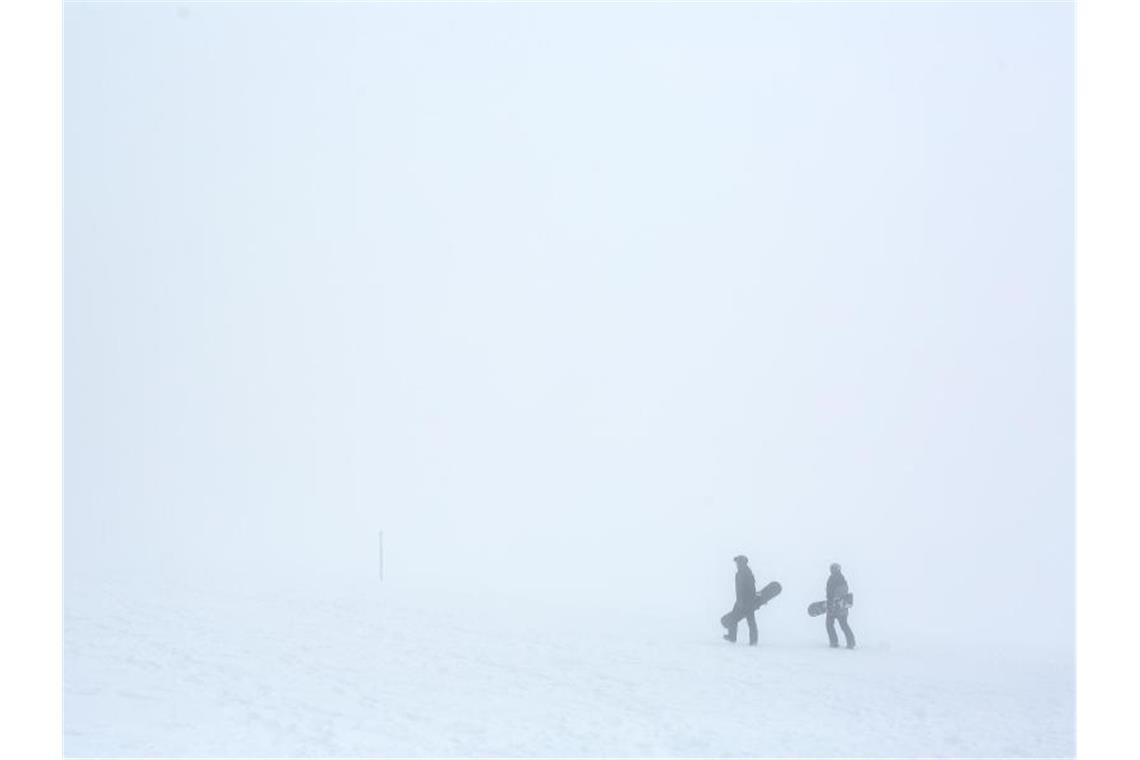 Zwei Snowboarder gehen im dichten Nebel durch den Schnee. Foto: Philipp von Ditfurth/dpa