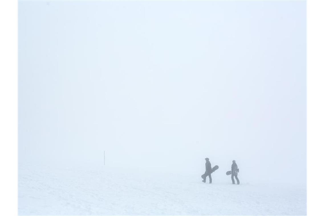 Frost und Schnee in Baden-Württemberg Zwei Snowboarder gehen im dichten Nebel durch die verschneite Landschaft. Foto: Philipp von Ditfurth/dpa
