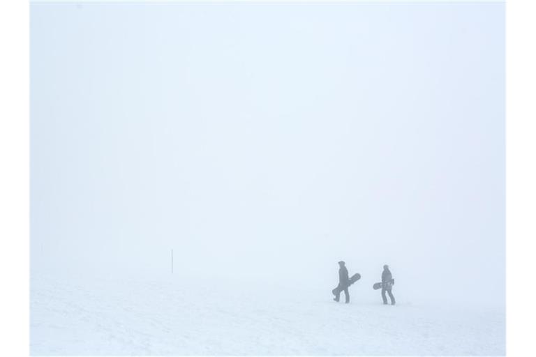 Zwei Snowboarder gehen im dichten Nebel durch die verschneite Landschaft. Foto: Philipp von Ditfurth/dpa