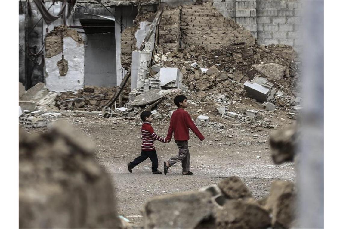 Zwei syrische Jungen gehen Hand in Hand an zerstörten Häusern vorbei. Foto: Mohammed Badra/epa/dpa